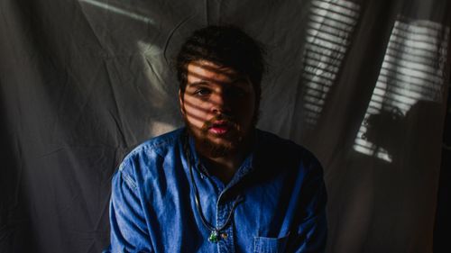 Portrait of young man against textile in darkroom