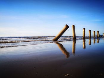 Wooden posts in sea against sky