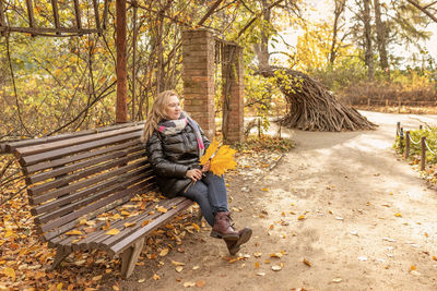 Portrait of a woman sitting on a bench in a gazebo entwined with a vine in an autumn park.