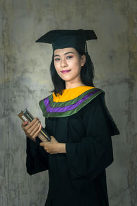 Portrait of smiling young woman holding smart phone standing against wall