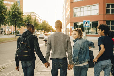 Rear view of male friends walking side by side on street in city