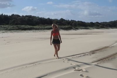 Full length of woman walking at sandy beach on sunny day