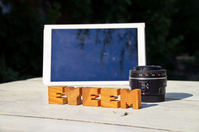 Close-up of wooden eyeem text by camera lens on table