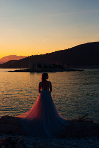 Woman standing on mountain by sea against sky during sunset