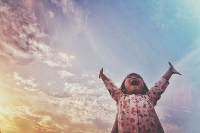 Low angle view of cheerful girl standing against sky