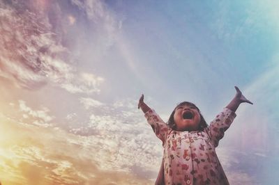 Low angle view of child standing on rock against sky