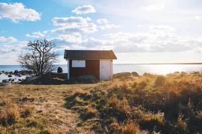 Scenic view of house on field by sea against sky