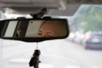Woman reflecting on rear-view mirror of car