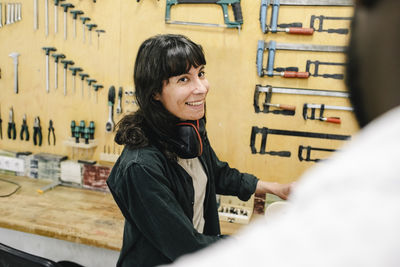 Smiling female technician with ear muffs talking with customer at repair shop