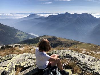 Rear view of woman sitting on rock against mountains