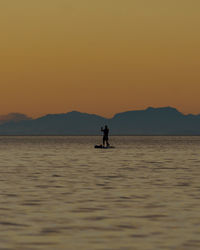 Silhouette man in sea against orange sky