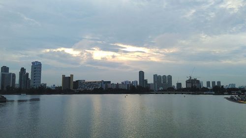 City at waterfront against cloudy sky