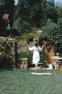 Rear view of woman standing against trees in garden 