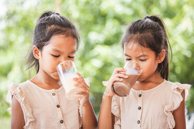 Friends drinking milk from glasses against trees