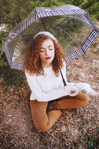 Young woman with umbrella sitting on field