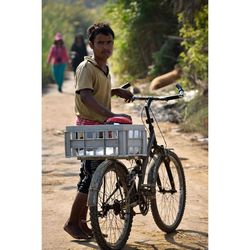 Portrait of vendor with bicycle standing on dirt road