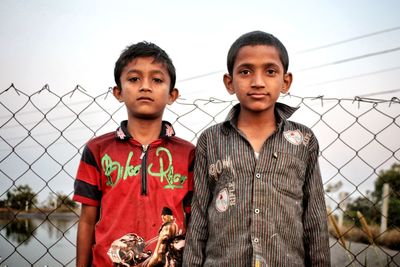 Portrait of boys standing against chainlink fence