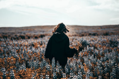 Rear view of woman standing amidst flowers on field