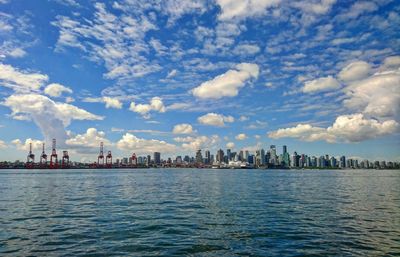 City at waterfront against cloudy sky