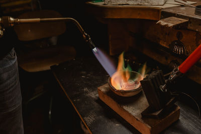 Unrecognizable goldsmith melting metal for jewellery with blowtorch while standing near workbench in workshop