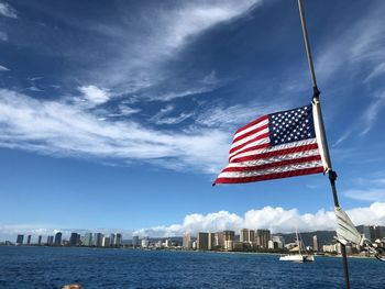 American flag waving by sea against sky in city