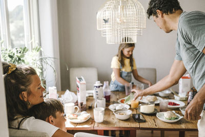 Mother and son embracing while father and daughter standing by at dining table