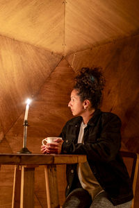 Woman having a cup of coffee sitting inside a dome tent.