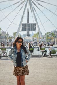 Young woman with hands in pockets standing against ferry wheel