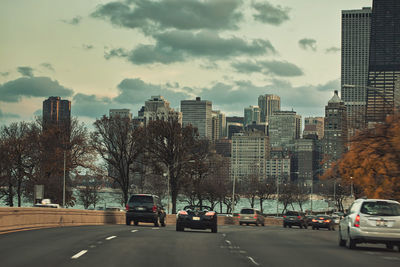 Cars on road by buildings in city against sky