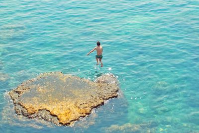 High angle view of shirtless man on rock in sea