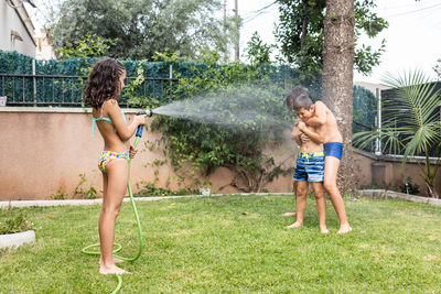 Three funny kids playing with a hose in the garden