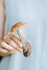 Crop woman in casual white wear holding freshly picked porcini mushroom with soil