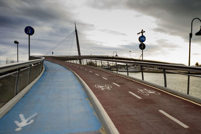 Pedestrian and bicycle lane signs on bridge against cloudy sky