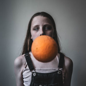 Portrait of young woman holding fruit against wall