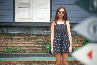 Portrait of a young woman standing against brick wall