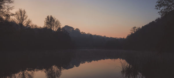 Reflection of silhouette trees in lake against sky during sunset