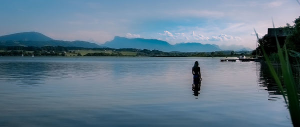 Rear view of woman standing in lake against sky during sunset