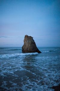 Rock formation in sea against clear blue sky