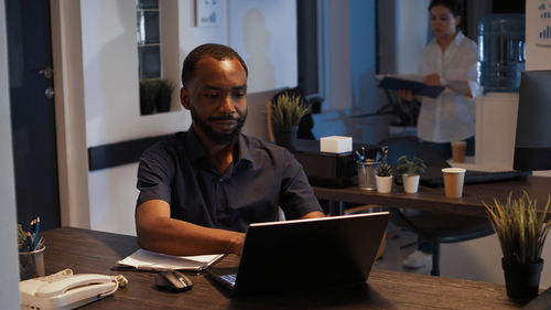 Portrait of young man using laptop at desk in office