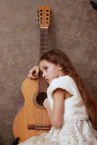 Sad girl sitting by guitar against wall
