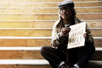 Beggar with text on cardboard sitting on steps