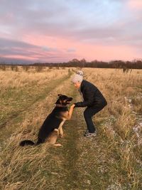 Side view of woman holding dog paw on grassy field