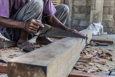 Low section of man cutting wood while sitting outdoors