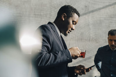 Young businessman using mobile phone while having tea at office