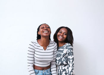 Cheerful african american females in casual clothes hugging and laughing in studio against white background