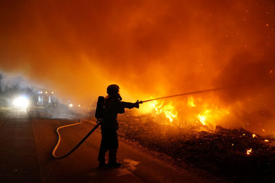 Silhouette man standing on illuminated fire at night