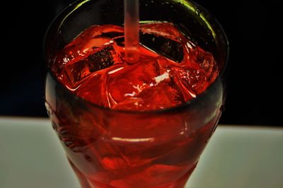 Close-up of fresh red drink with ice cubes and straw on table