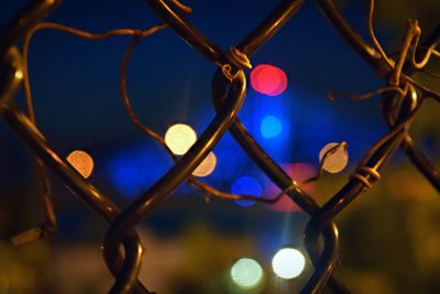 Close-up of illuminated defocused lights seen through fence at night