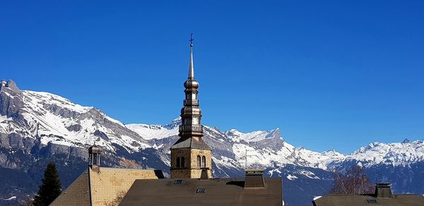 Snow covered buildings and mountains against clear blue sky