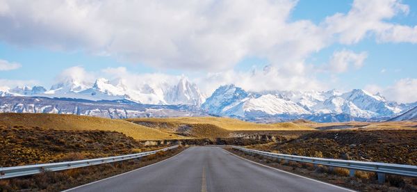 Panoramic view of empty road amidst snowcapped mountains against sky